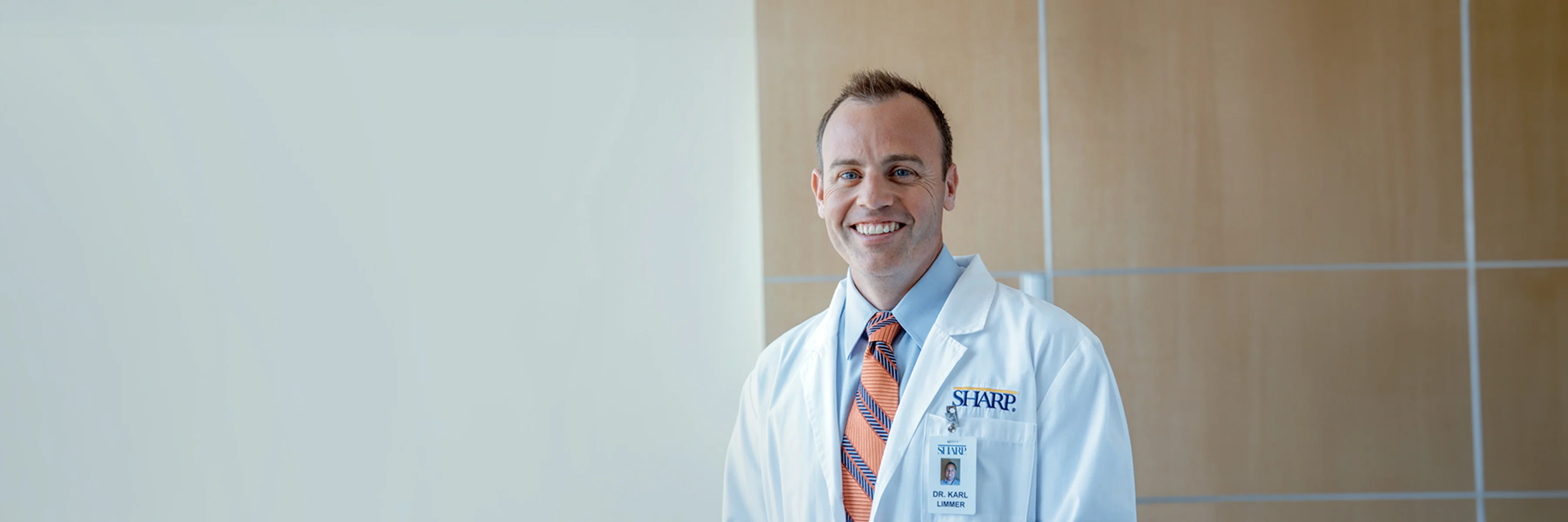 Dr. Limmer smiling in white coat and orange/blue striped tie.