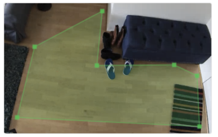 An indoor camera screenshot of a living room and a diagonal green arrow that indicates the tripwire.