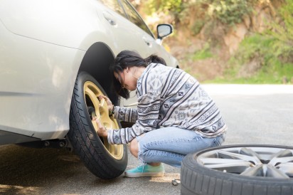 Autoversicherung Reifenplatzer: Frau wechselt platten Reifen
