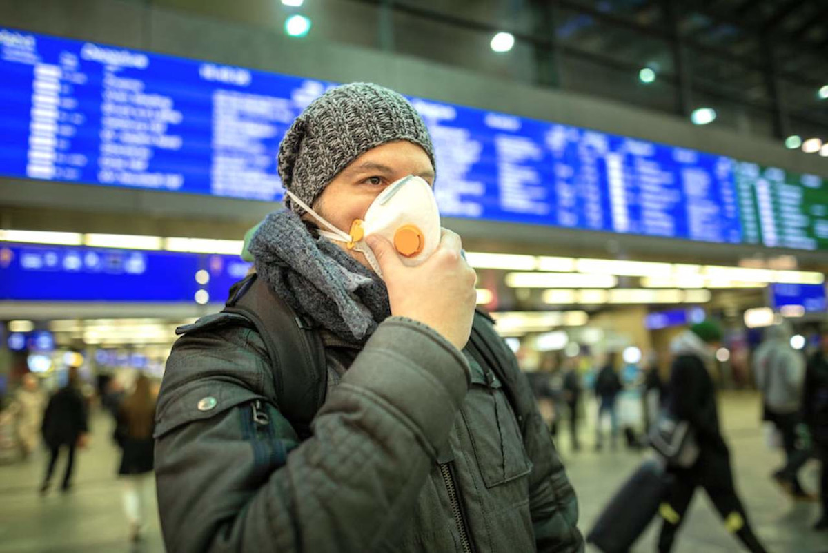 Ein Mann steht zu Beginn der Coronapandemie mit Mundschutz auf einem Bahnhof.