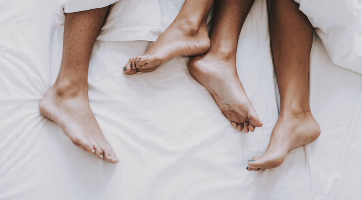 Unter einer Bettdecke schauen männliche und weibliche Füße hervor.
