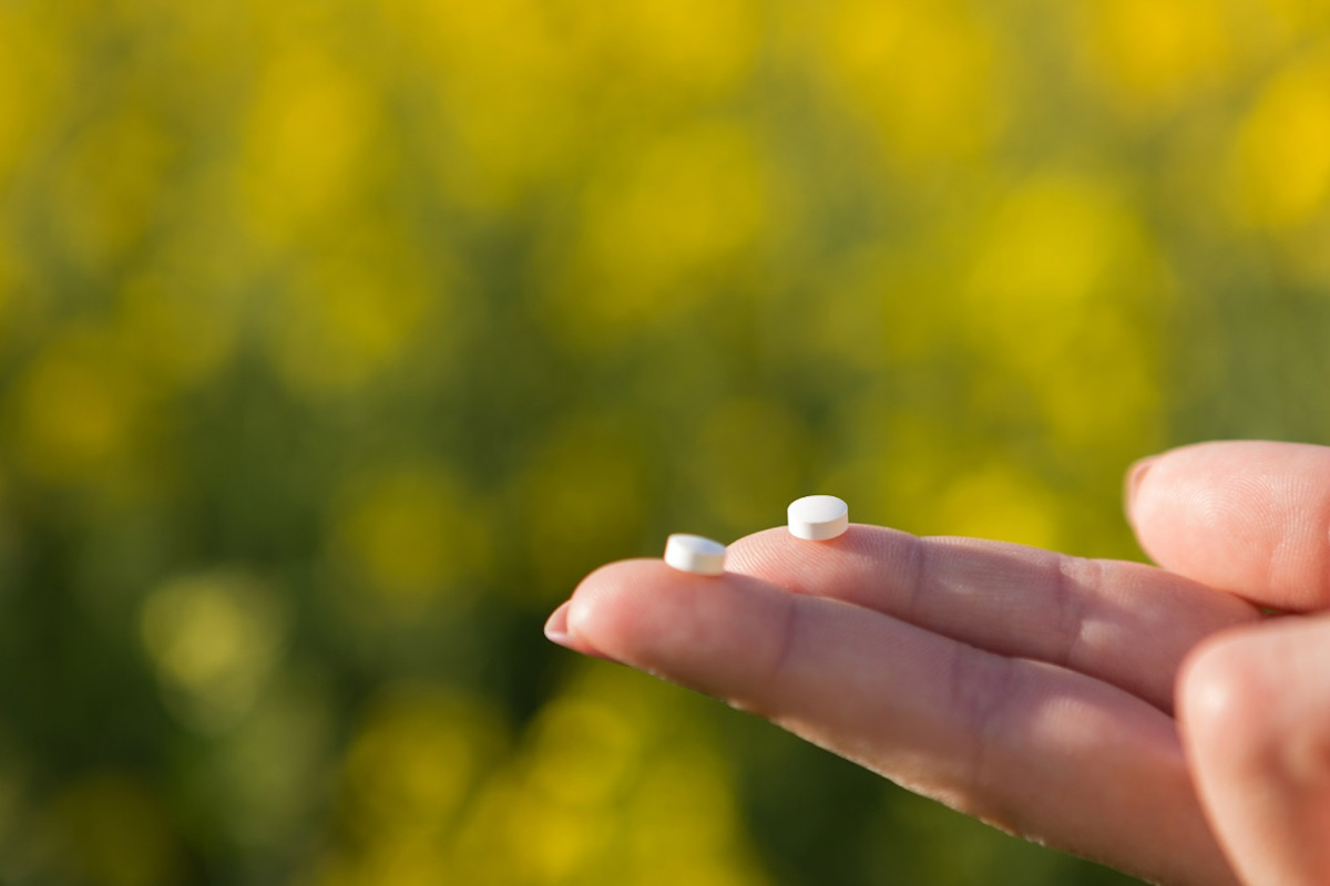 Zwei kleine weiße Tabletten werden auf den Fingerspitzen gehalten.