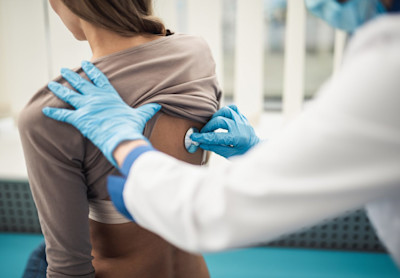 Ein Arzt hört mit dem Stethoskop am Rücken einer Patientin die Lunge ab.