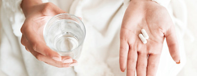 Antibiotika Tabletten in Hand und ein Glas Wasser dazu.