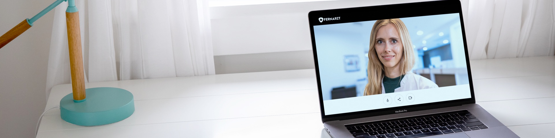 Panoramaansicht Notebook auf Schreibtisch. Auf dem Display ist eine Ärztin zu sehen.