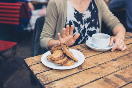Eine Frau trinkt Kaffee und lehnt das angebotene Brot ab.