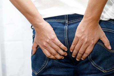 Person in Jeans hält sich den Po mit beiden Händen.