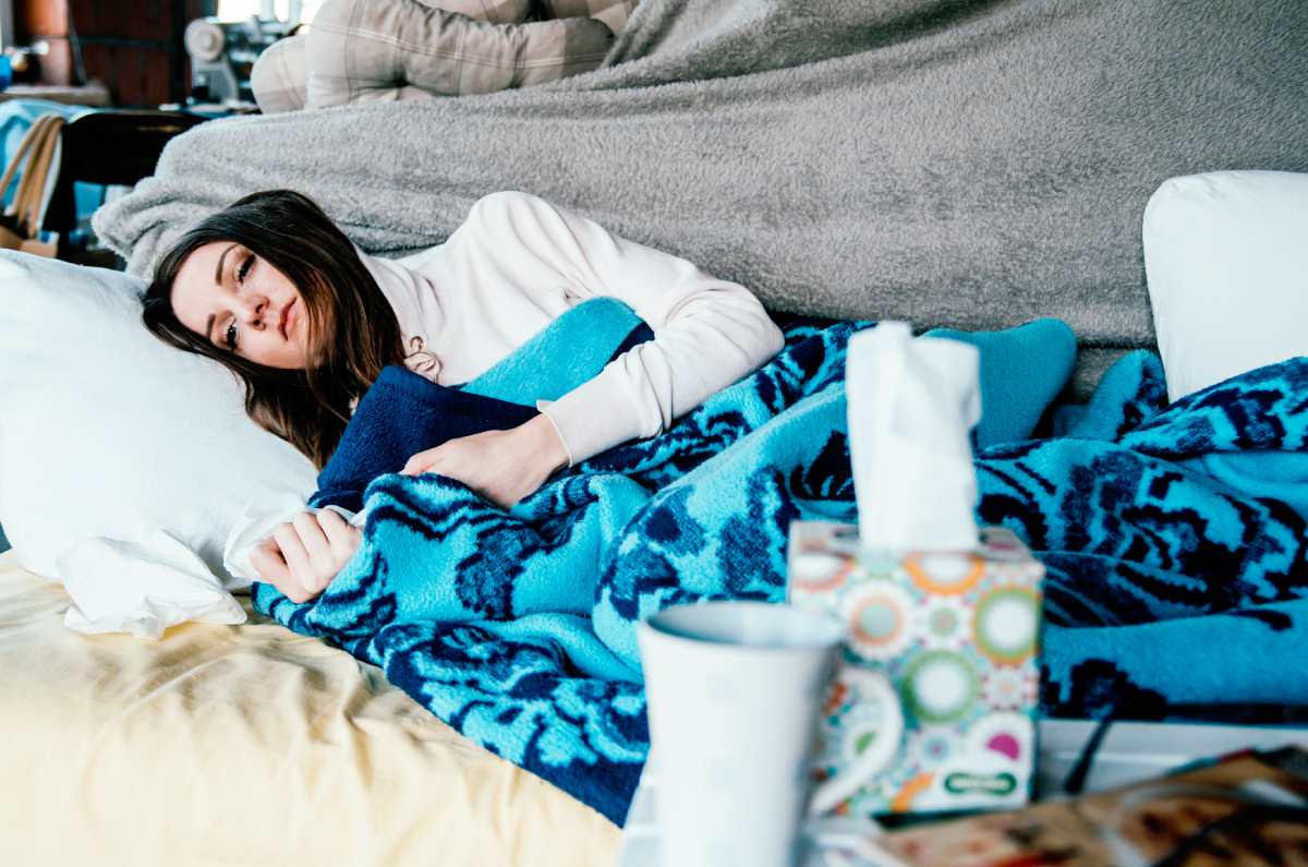 Eine Frau liegt krank auf dem Sofa.