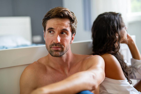 Es ist ein junges Paar im Bett zu sehen. Sie sind voneinander abgewendet.