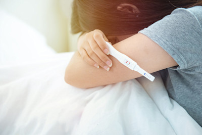 Frau hält Schwangerschaftstest und vergräbt ihr Gesicht in den Armen.