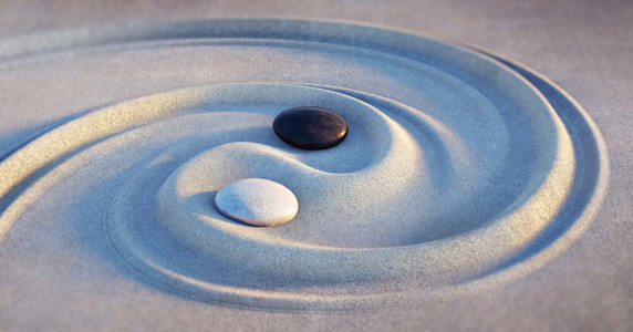 Ying und Yang wurde in den Sand gezeichnet. Die Symbolik wird durch einen schwarzen und einen weißen Stein verdeutlicht.
