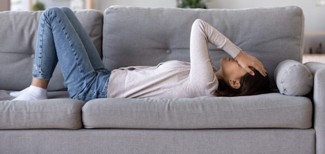 Eine Frau hat vestibuläre Migräne und liegt mit Kopfschmerzen und Schwindel auf dem Sofa.