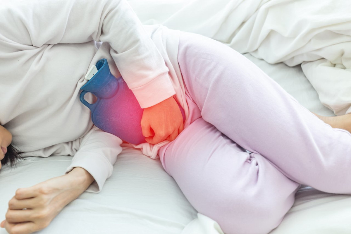 Eine Frau hat Schmerzen im Unterbauch und lindert diese mit einer Wärmflasche.