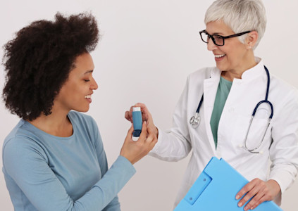 Eine Ärztin reicht einer Patientin mit Asthma einen Inhalator.