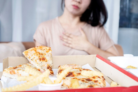 Frau hält sich die Hand an das Brustbein, nachdem sie Pizza und Pommes gegessen hat.