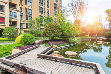 Eine Brücke führt über einen See. Im Hintergrund befindet sich ein mehrstöckiges Haus.