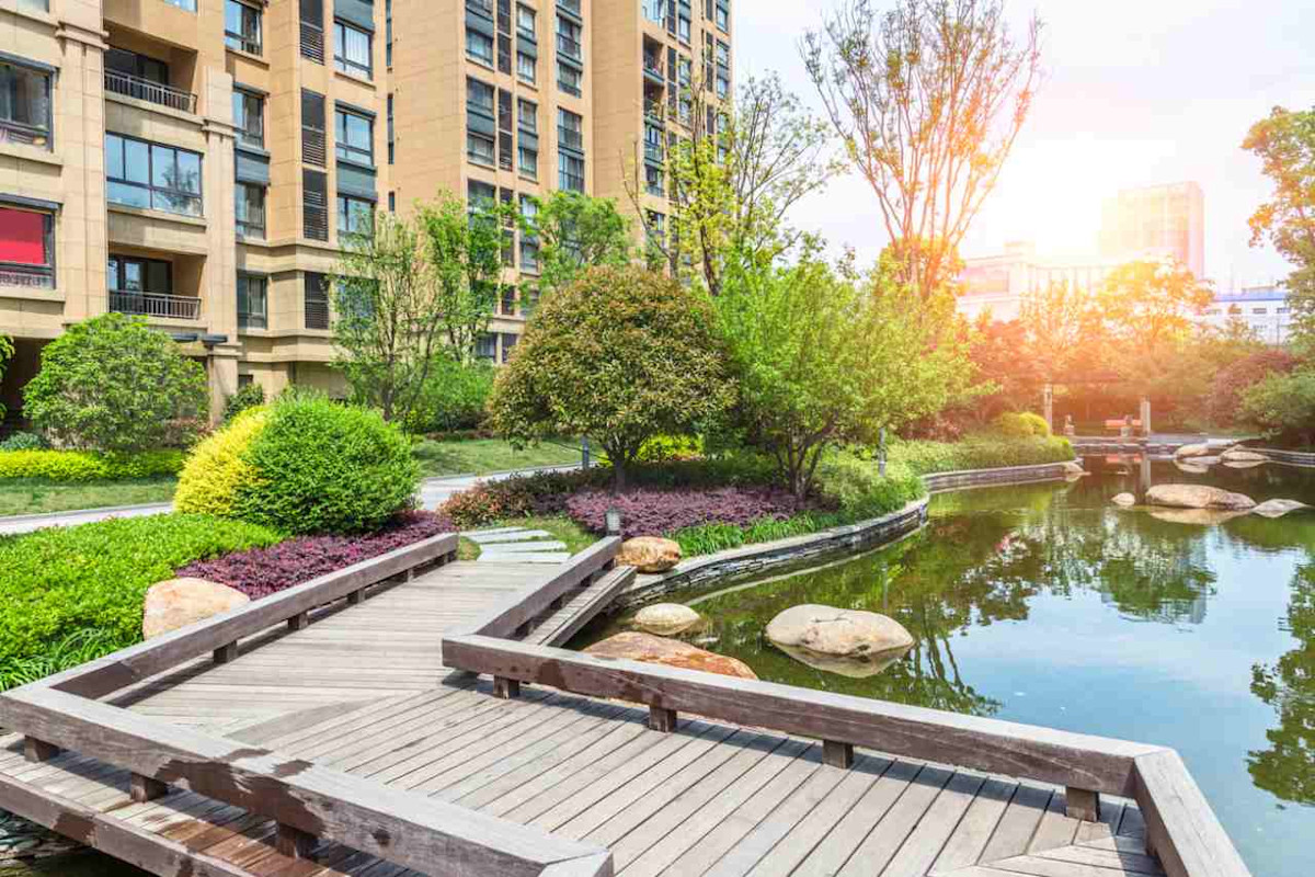 Eine Brücke führt über einen See. Im Hintergrund befindet sich ein mehrstöckiges Haus.