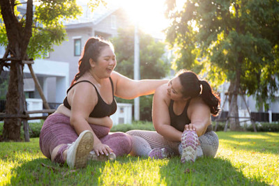 Zwei Übergewichtige Frauen machen Yoga-Übungen im Park und haben Spaß dabei.