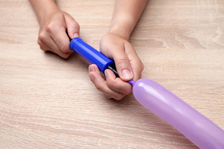 Ein länglicher Luftballon wird mit einer Luftpumpe befüllt.