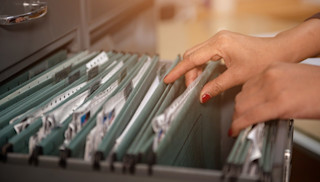 Frauenhände blättern durch Patientenakten in einem Hängeregister.