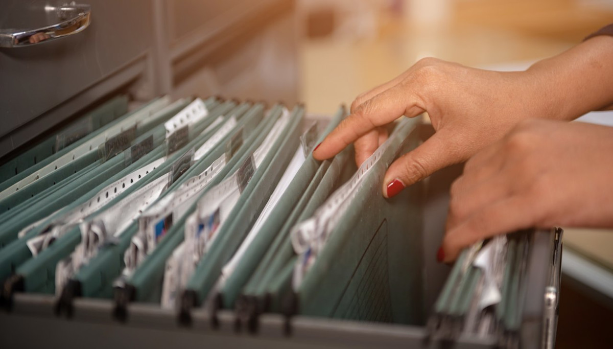 Frauenhände blättern durch Patientenakten in einem Hängeregister.