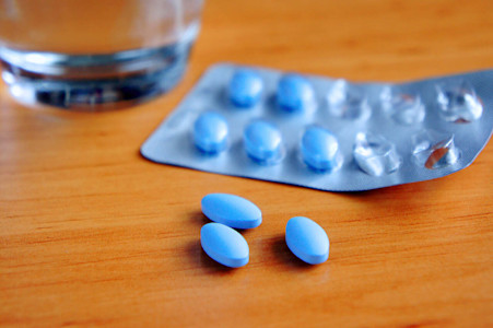 Blaue Tabletten in einem Blister liegen auf einem Holztisch, im Hintergrund steht ein Glas Wasser.