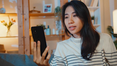 Junge Frau hält Smartphone in der Hand und führt ein Videotelefonat.