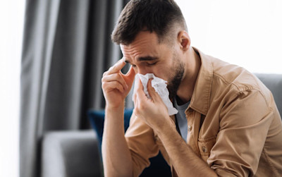 Mann mit Nasennebenhöhlenentzündung (Sinusitis) und Schnupfen schnäuzt sich in ein Taschentuch.
