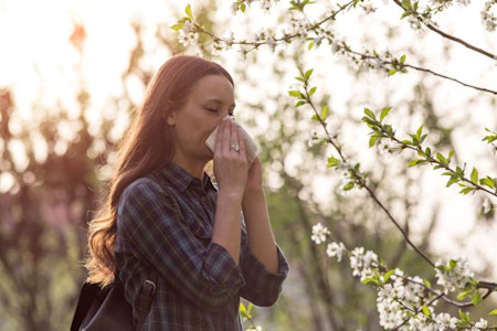 Frau Nase putzend zwischen Baumblüten