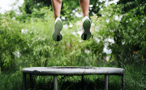Beine beim Hochspringen auf einem Trampolin im Grünen.