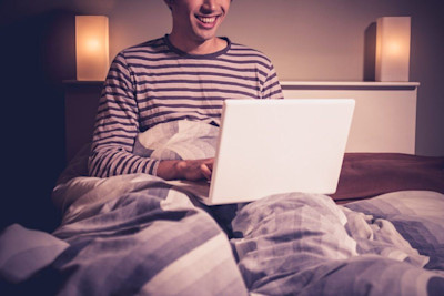 Glücklicher Mann mit Laptop im Bett.