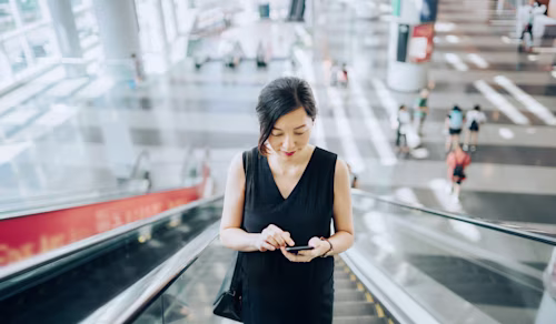 エスカレーターに乗ってスマートフォンでメールをチェックする女性