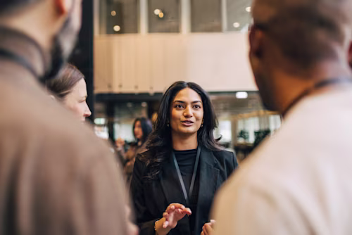 Joven emprendedora discutiendo con delegados durante un evento de networking en el centro de convenciones.