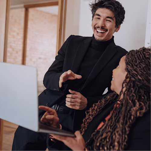 Two people smiling and having a conversation while holding a laptop