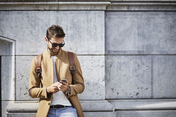 Smiling man in camel coat looking at mobile phone