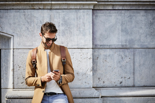 Smiling man in camel coat looking at mobile phone