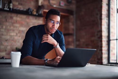 Focused Professional Working on Laptop in a Modern Brick Office Space.