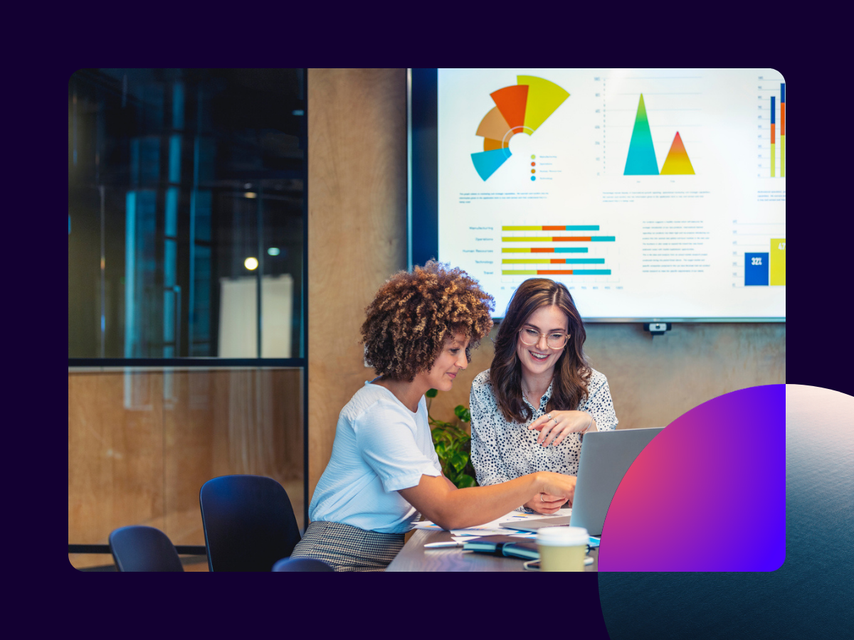 Two women working in a conference room with charts on the wall.