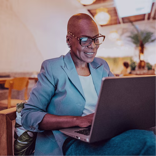 A seated black woman smiling while working at her laptop