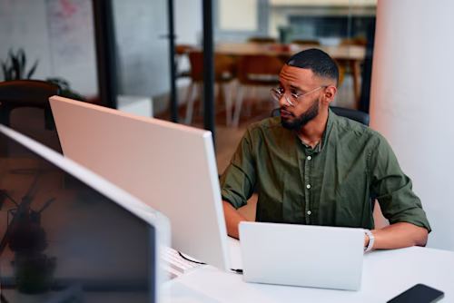 Focused young programmer working on multiple devices in a modern office