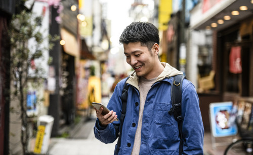 Cheerful young man looking at smartphone in street