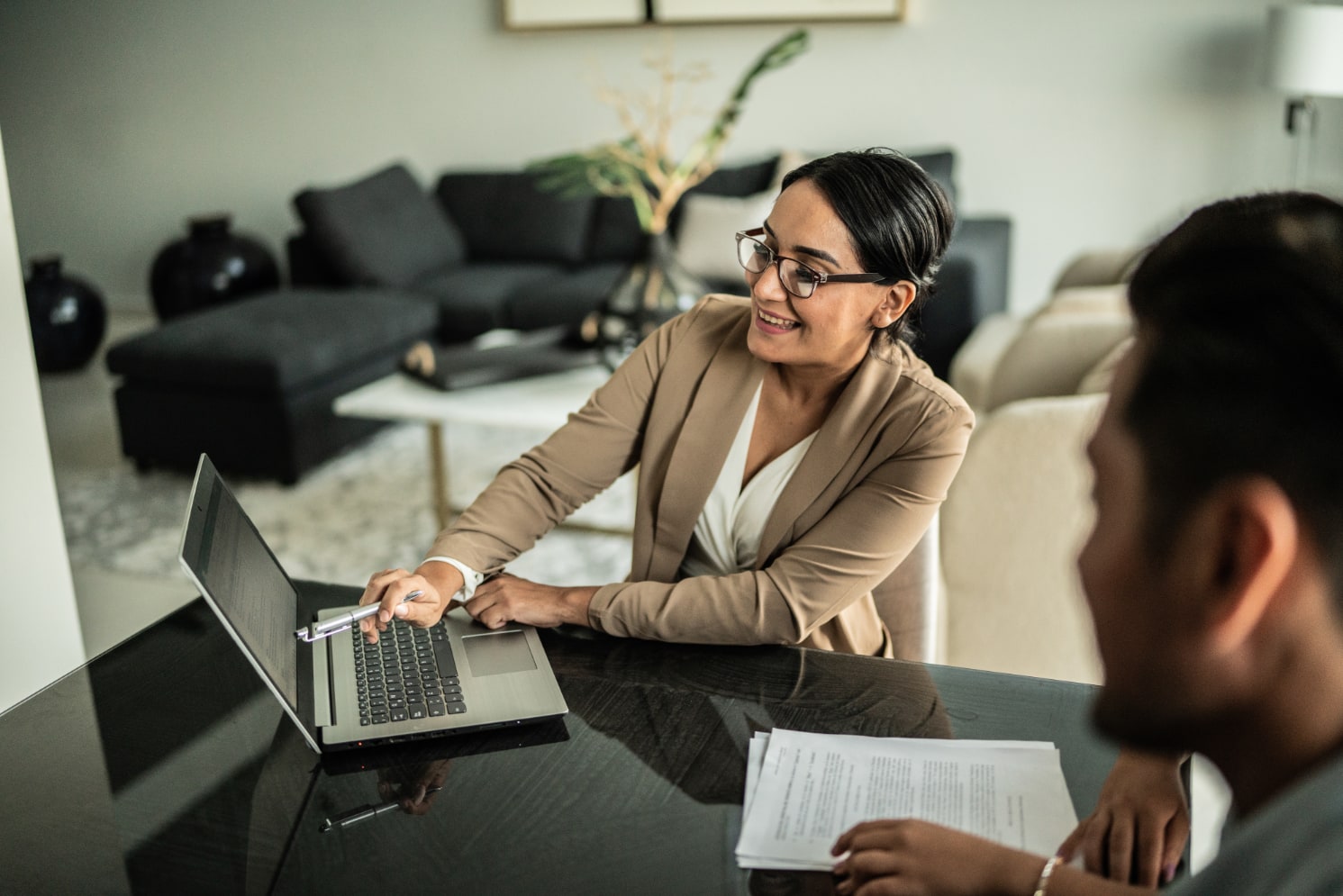 A woman smiling while working on a laptop with a colleague.