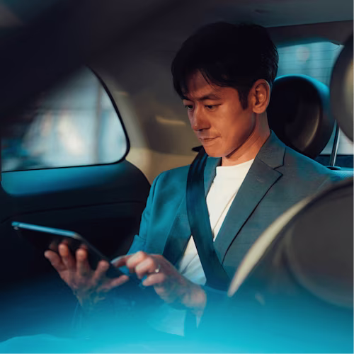Man in suit working on a tablet from the backseat of a car