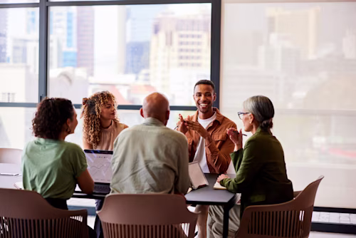 Cheerful mid adult man smiling and talking to four business colleagues in meeting