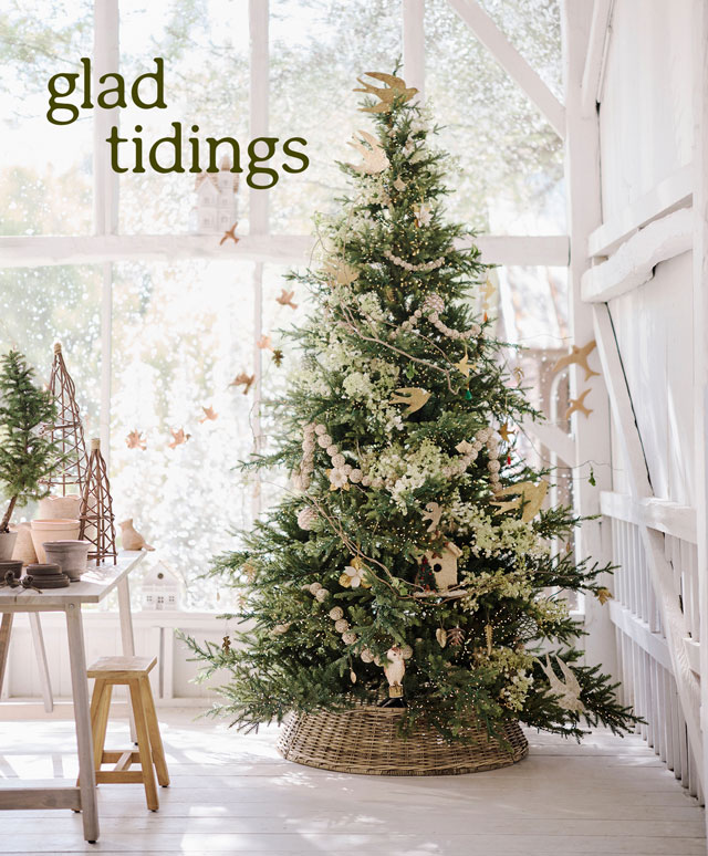 Bright white sunroom with decorated Christmas tree, white furniture, and snowy windows displaying glad tidings text.