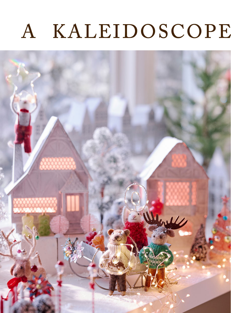 Festive winter village scene with illuminated snow-covered houses, decorative animal figurines, and twinkling lights.