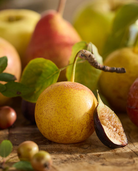 Yellow pear with stem and sliced section showing flesh, surrounded by whole pears and green leaves on wooden surface.