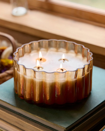 Gold and white striped decorative candle with four lit wicks in a fluted glass container on a teal surface.