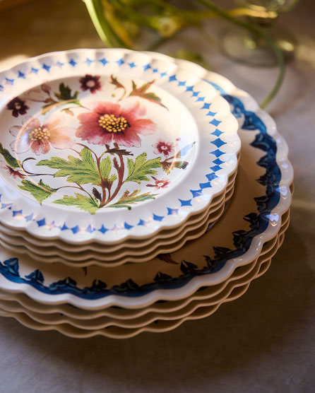 Stack of decorative ceramic plates with scalloped edges, featuring hand-painted floral designs in pink, green, and blue patterns.