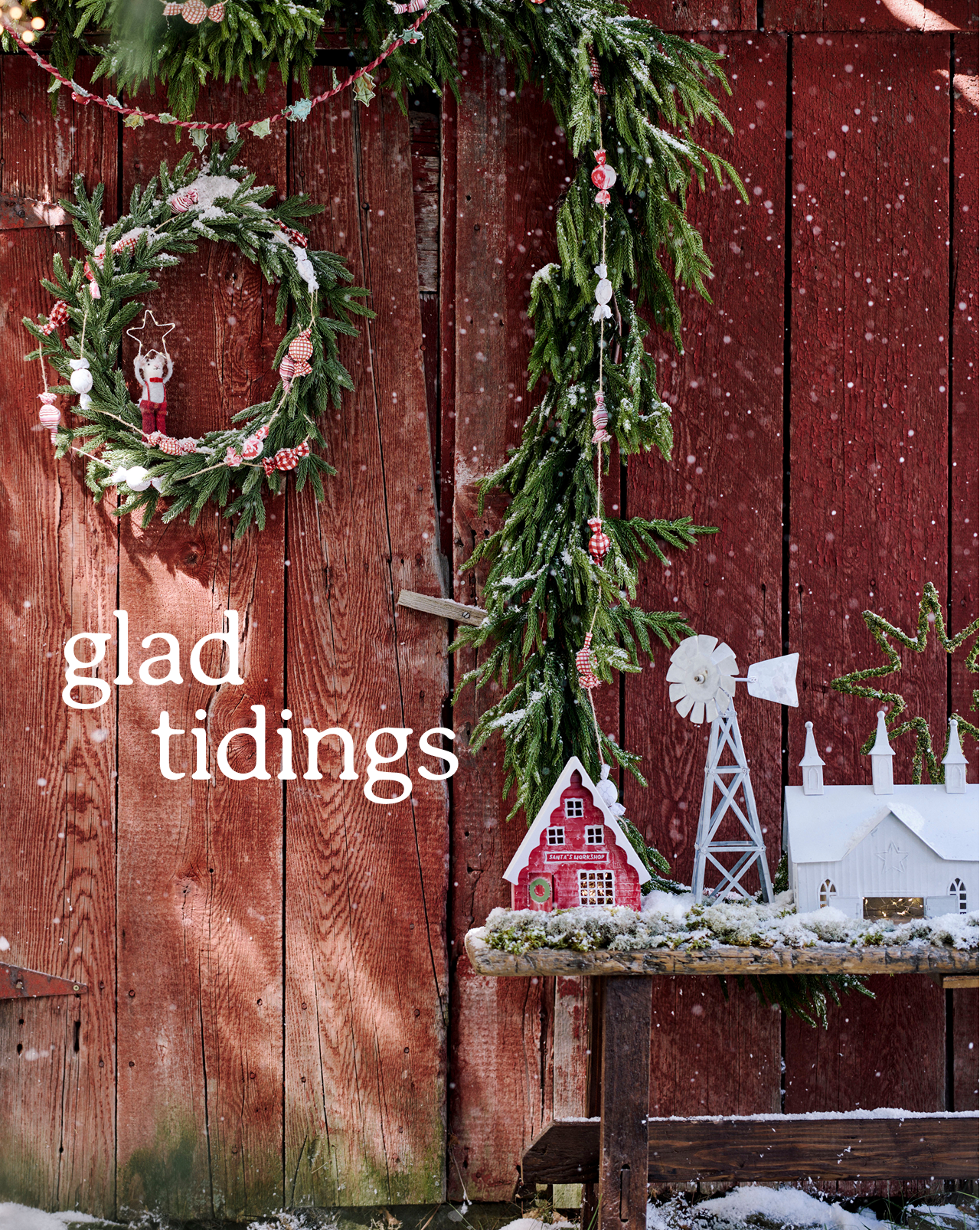 Miniature Christmas village scene with red barn, white church, windmill, and green star decoration on rustic wood with snow.